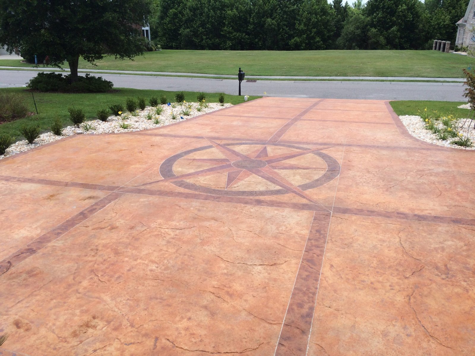 Buildgreen Industries created a residential decorative concrete driveway with a stamped pattern that makes the concrete look like stone and a compass rose design in the center