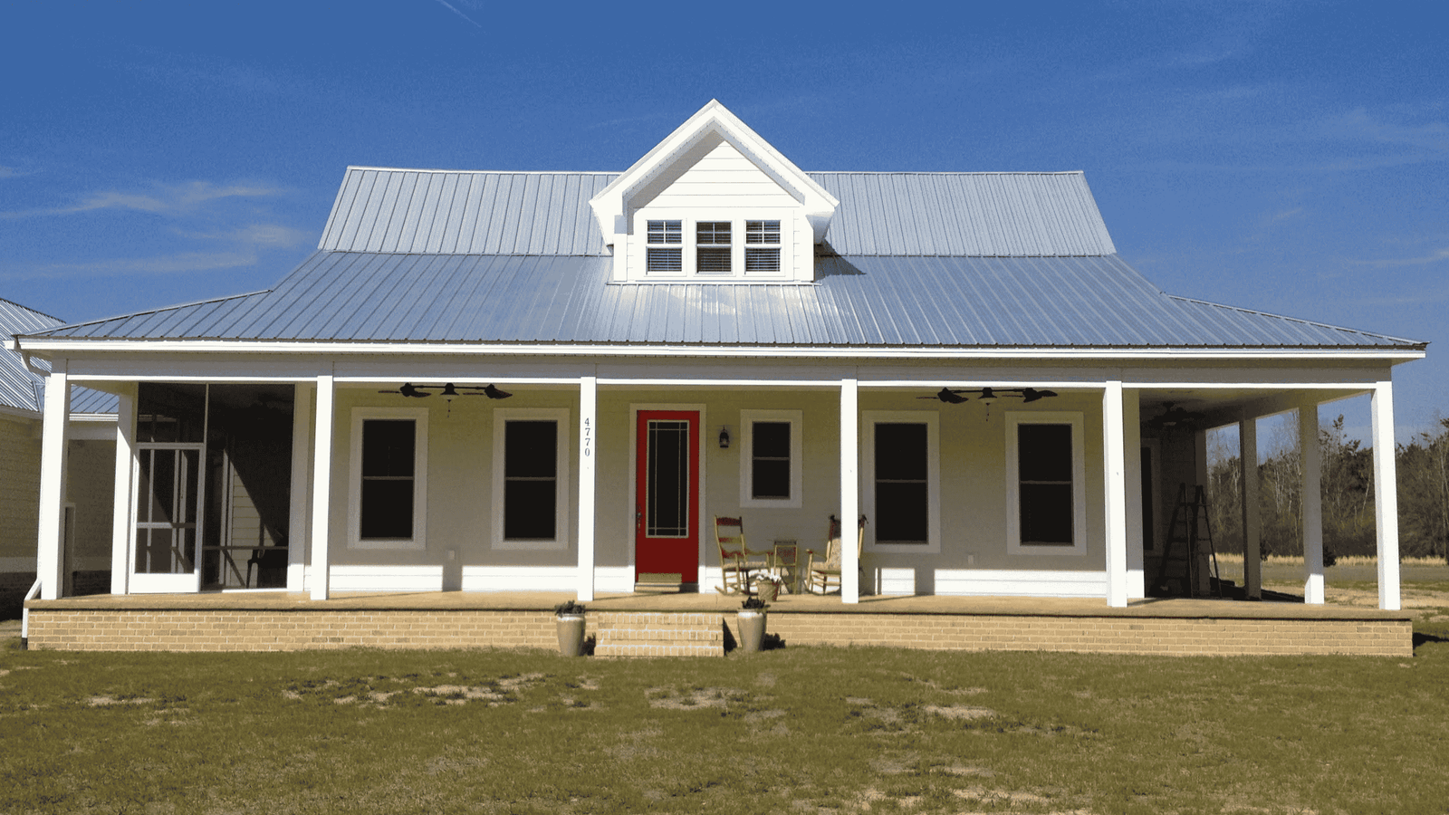 An energy-efficient South Carolina house with a porch, a metal roof, and a dormer window. Though it is not obvious on the surface, it has concrete walls beneath and is built using a variety of green building techniques.