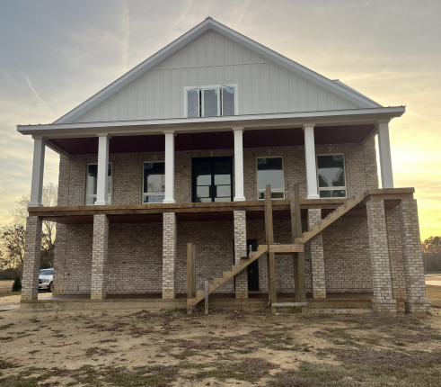 In-progress concrete house with two layers of porches. Wooden stairs lead up to the unfinished second porch.