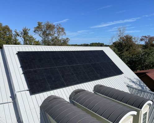The metal roof of a house with a dark-colored solar panel on a sunny day with a blue sky.