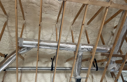 A ceiling covered in a fluffy material - spray foam. We can also see ducts and wood.