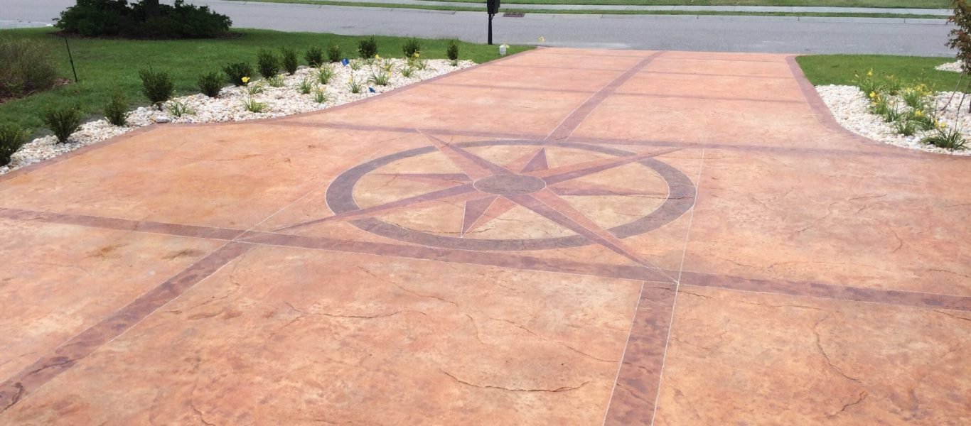 A residential decorative concrete driveway with a stamped pattern that makes the concrete look like stone and a compass rose design in the center