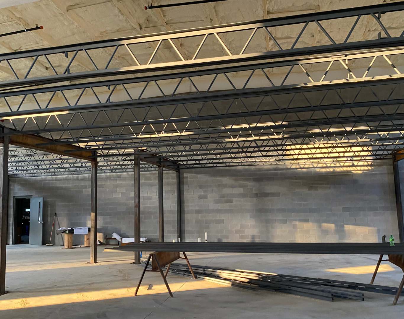 A commercial office under construction at sunset with exposed metal beams and spray foam insulation on the ceiling.