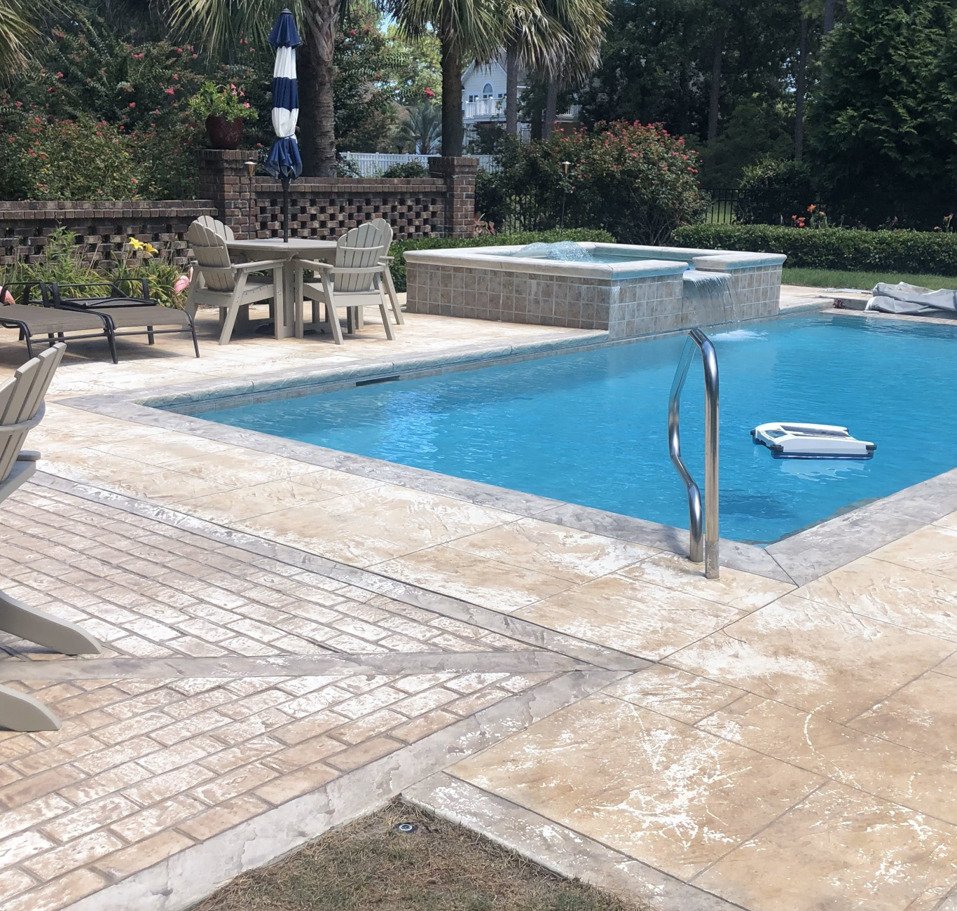 Pool with decorative concrete paver patio designed to look like stone in South Carolina, SC by Buildgreen Industries. The pool is surrounded by palm trees and pool chairs.