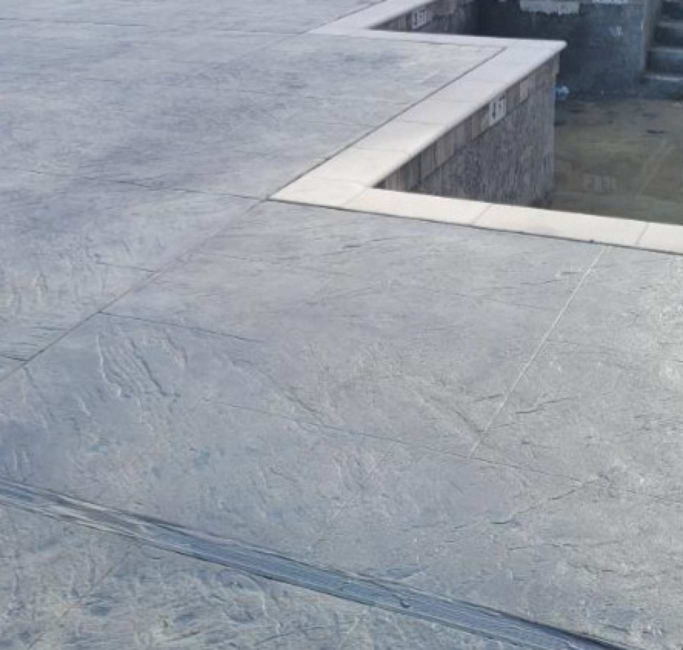 Decorative concrete stamped to look like stone surrounded a geometric pool.
