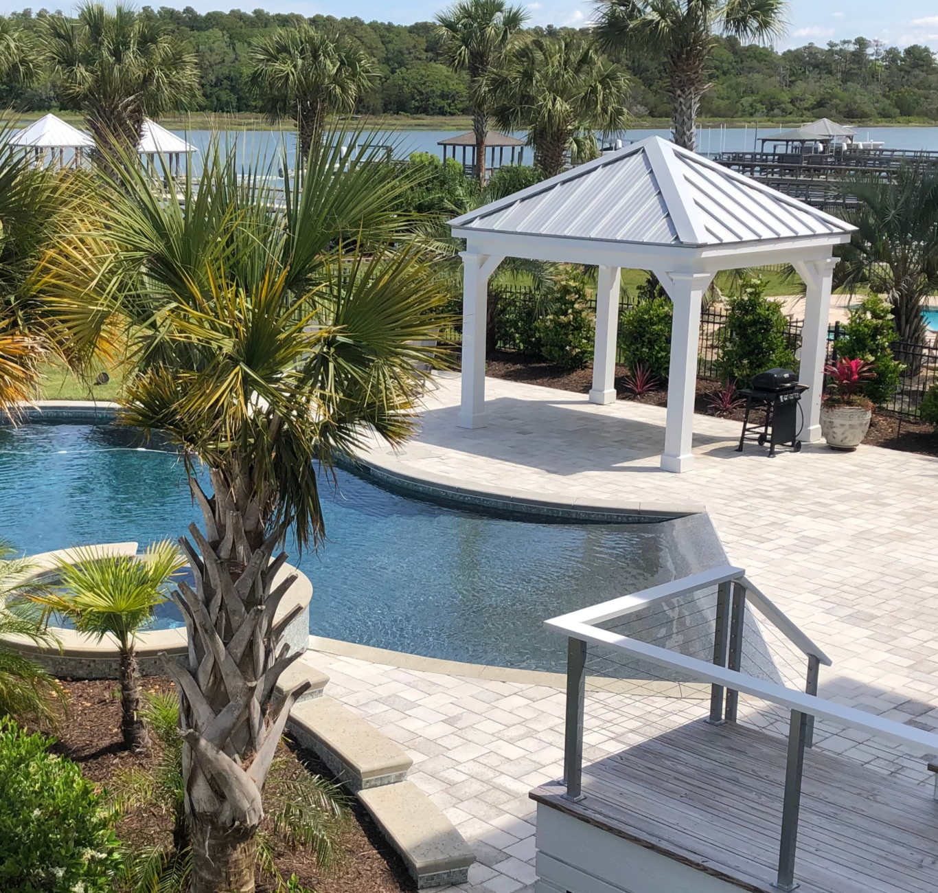 A sunlit concrete patio surrounding a pool and featuring a gazebo and palm trees